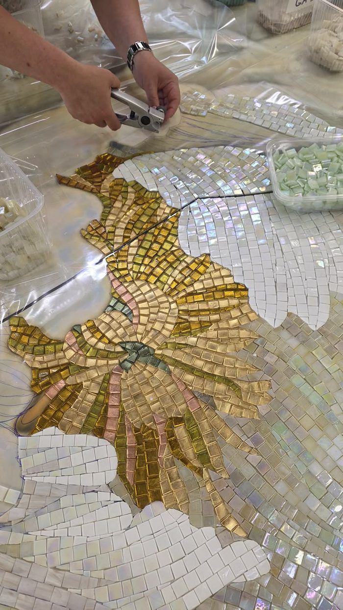 Mosaic artist hand-cutting gold glass tesserae with nippers while assembling a radiant mosaic